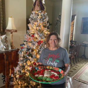 Nana holding a tray of her famous sugar cookies in front of a beautifully decorated Christmas tree, smiling warmly as she shares her beloved holiday tradition.