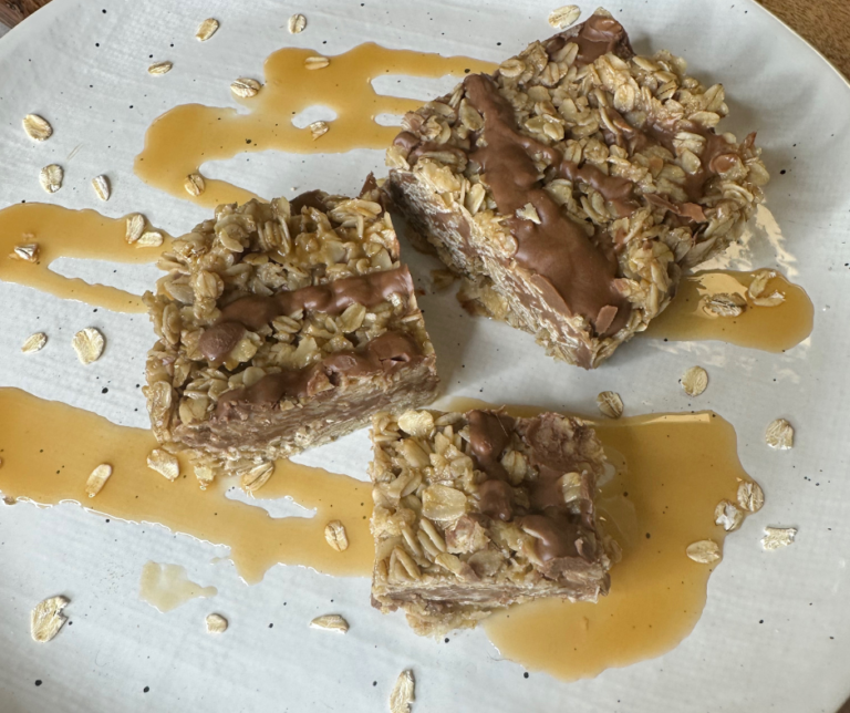 a-square-no-bake-chocolate-oat-bar-on-a-white-plate-with-chocolate-chips-the-bar-has-a chewy-texture-and-is-made-with-rolled-oats-and-peanut-butter