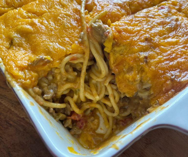 A close-up photo of a delicious cheesy taco spaghetti bake in a casserole dish with melted cheese on top