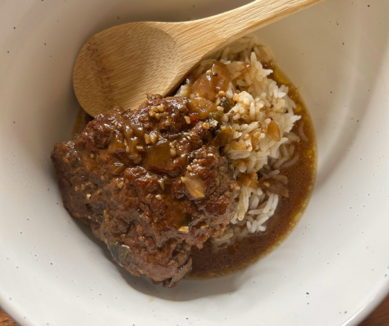 A photo of a classic hamburger steak and gravy dish on a white plate, with brown gravy covering the steak and rice