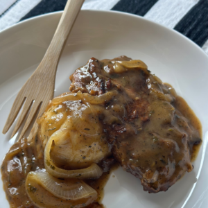 Golden-brown skillet-seared pork chops topped with rich, sweet onion gravy, served over a fluffy bed of creamy mashed potatoes, garnished with fresh herbs for a comforting and hearty presentation.